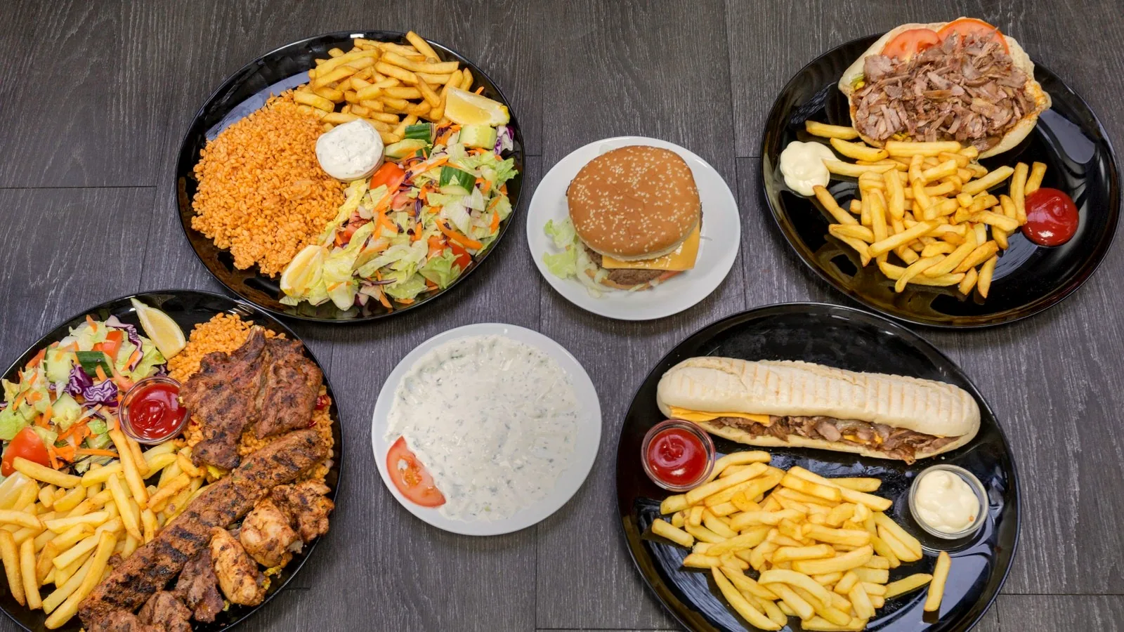 Assiettes avec frites, boulghour et crudités, grillades, cheeseburger, sandwich kebab et panini, servis sur des assiettes noires